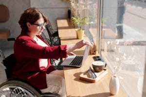 A blogger in a wheelchair using a laptop, exploring how to get paid and start their own blog.