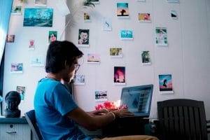 A teenager sitting in front of a laptop with pictures on the wall, following the ultimate guide on how to make money without a job.
