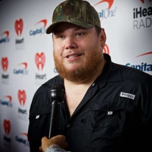 A bearded man in a hat is holding a microphone at Luke Combs' concert.